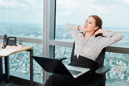 Tired young businesswoman with stiff neck leaning back in her chair after finishing workの写真素材