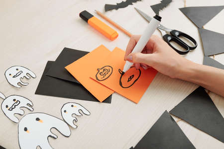 Creative woman drawing Halloween symbols on colorful paper to cut them out and hang around for the celebrationの写真素材