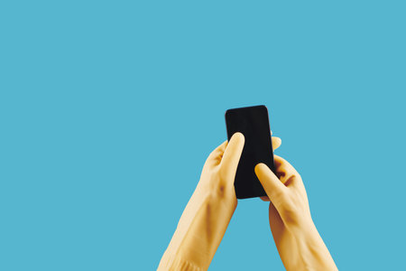 Housewife in yellow rubber gloves using mobile appication on smartphone, isolated on blue
