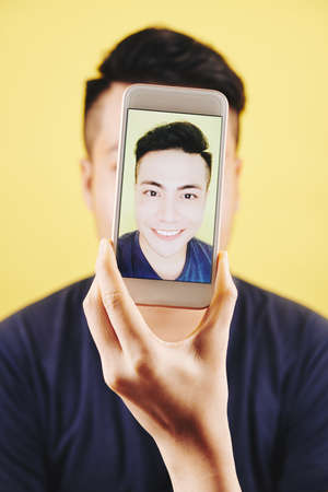 Smiling handsome Vietnamese man taking selfie on smartphone in his handの写真素材