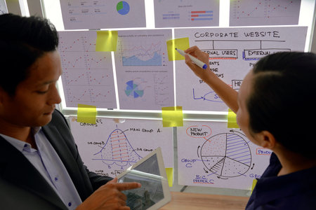 Businessman analyzing chart on tablet computer and telling female coworker what to write of stickers