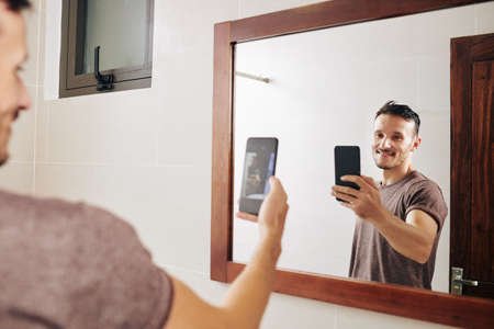 Smiling attractive fit Caucasian man taking selfie at bathroom mirrorの写真素材
