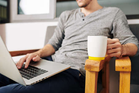Man sitting in chair with big mug of coffee and working on new website for his companyの写真素材