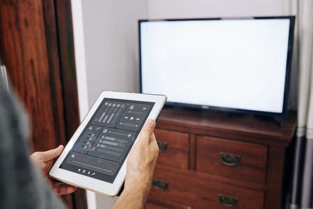 Man using application on tablet computer to change channels and volume on tv setの写真素材