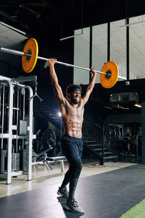 Excited happy Black muscular man practicing weight lifting in gymの写真素材