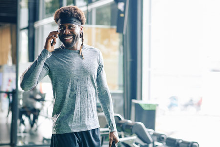 Portrait of handsome young Black man talking on phone after intense training in gym