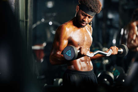 Fit Black man doing biceps exercise with EZ curl bar in gymの写真素材