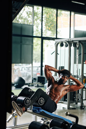 Young shirtless strong fit man doing crunches on gym bench
