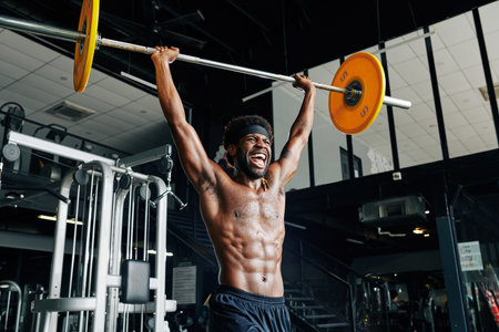 Fit sweaty Black man shouting when lifting heavy barbell high above his head