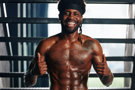 Portrait of happy handsome fit young Black man with defined abdominal muscules showing thumbs-up...