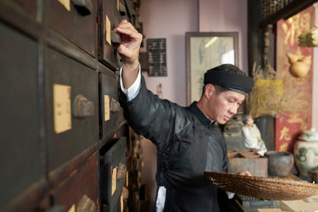 Traditional Asian herbal medicine practitioner opening drawers and filling bowl with ingredients for remedyの写真素材