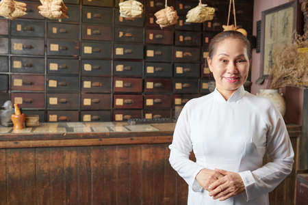 Portrait of smiling Asian woman in white traditional dress standing at traditional Chinese pharmacyの写真素材
