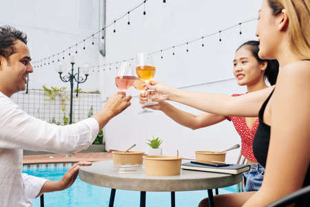 Group of start-uppers sitting at cafe table by the pool and toasting with wine glasses after discussing ideas for development of new projetcの写真素材