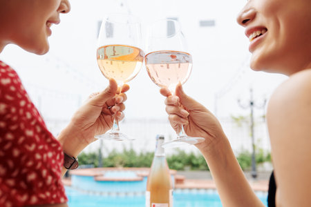 Glasses of sparkling wine in hands of smiling young women relaxing by swimming pool