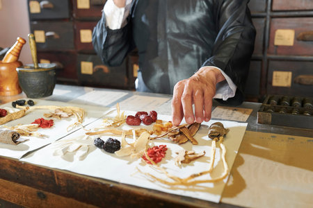 Traditional Chinese medicine practitioner talking on phone when packing dry roots and berries in...