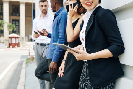 Cropped image smiling businesswoman standing outdoors with coworkers and reading information of digital tableの写真素材