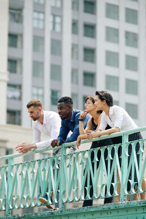 Business people spending time together outdoors, standing on bridge and leaning on handrailingの写真素材