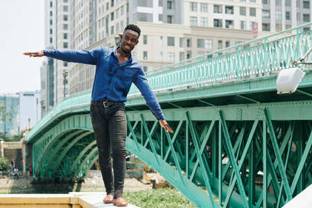 Smiling young Black businessman balancing with his arms when walking on granite borderの写真素材