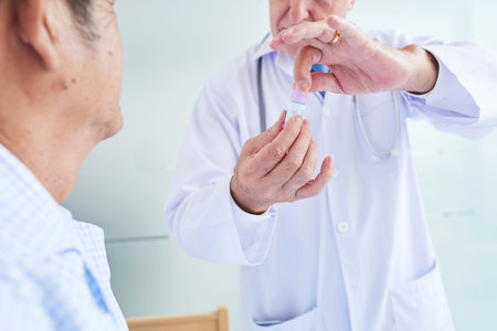 Close-up image of doctor showing small bottle of eye drops to senior patient and explaining how to...