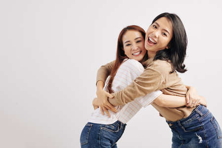 Portrait of young happy Vietnamese women hugging and looking at cameraの写真素材