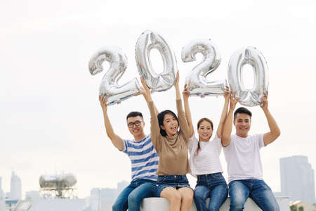 Portrait of cheerful young Vietnamese people raising hands with foil balloonsの写真素材