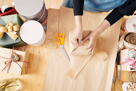 Hands of woman using sticky tape when wrapping gift box in decorative paperの写真素材