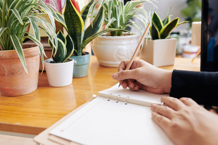 Hands of small flower shop owner writing down her plans and ideas in notebook
