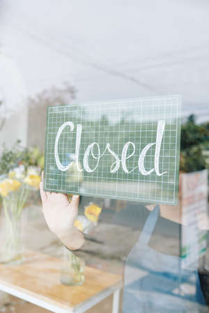 Close-up image of saleswoman turning signboard hanging on glass door when closing her small storeの写真素材