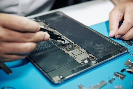 Close-up image of repairman using tweezers to installing microchip in tablet computer