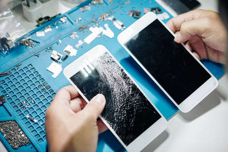 Cracked and news smartphone screens in hands of repairman, view from aboveの写真素材