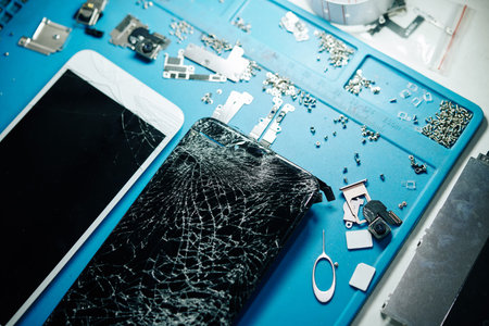 Two smartphones with broken screens and small screws on table of repairman, view from above