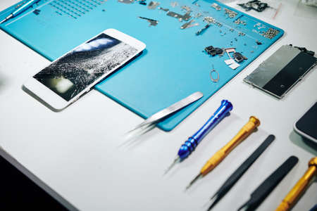 Smartphone with smashed screen, tools and details on desk of repairmanの写真素材