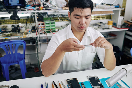 Young Asian repairman taking photo of smartphone with removed screen