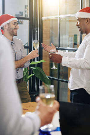 Multi-ethnic business people in Santa hats drinking champange and talking at Christmas party in officeの写真素材