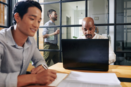 Mixed-race businessman sitting at table in meeting room and reading e-mails on laptop screen