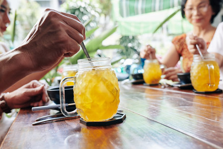 Hand of cafe visitor sitting at table and mixing sweet pineapple cocktailの写真素材