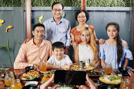 Happy big Vietnamese family posing at big dinner table for photo on smartphoneの写真素材