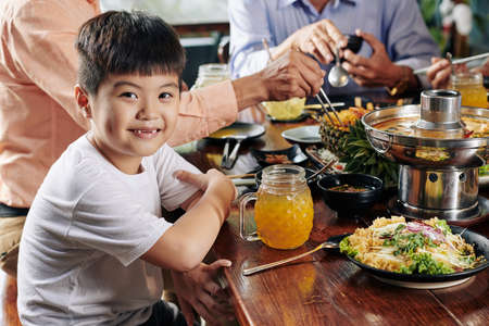 Portrait of smiling little Asian boy eating tasty dishes of Vietnamese cousine at family dinnerの写真素材