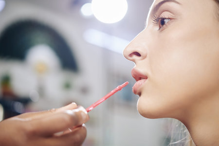 Close-up image of make-up artist applying liquid lipstick on beautiful modelの写真素材