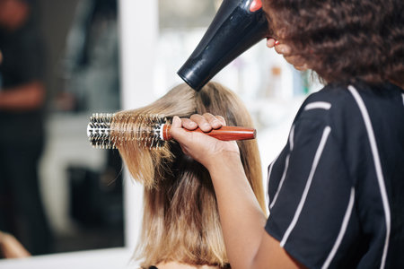 Professional stylist brushing and blowdrying hair of female client, view from the back