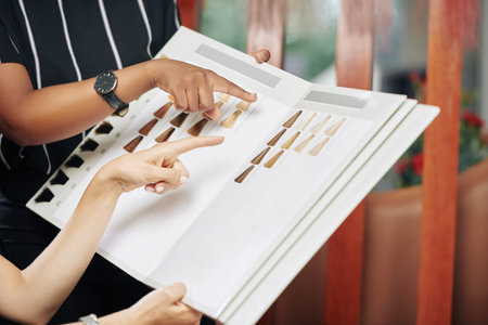 Hands of hairdresser and client choosing hair dye from samples in catalog, selective focus