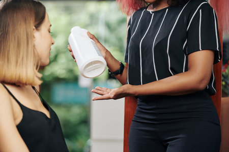 Cropped image hairdresser holding big bottle and describing benefits of new hair treatment to clientの写真素材