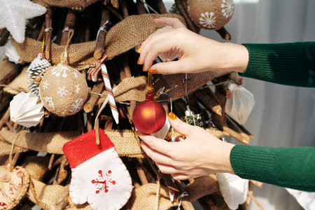 Hands of young woman hanging red bauble on Christmas tree