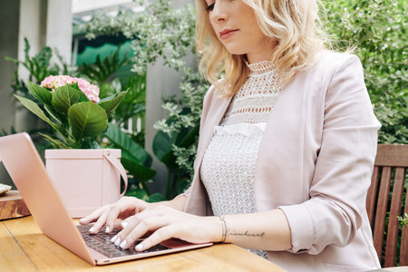 Cropped image of serious businesswoman working on laptop and answering e-mails from clients