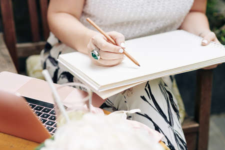 Close-up image of businesswoman drawing logotype or sketch with pencil in her sketchbook when sitting outdoors at tableの写真素材