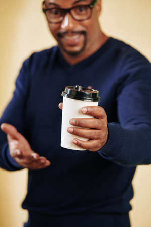 Cheerful Black man giving disposable cup with hot coffee, selective focusの写真素材