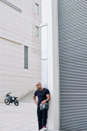 Positive handsome fit man in casual clothes standing with his motorcycle helmet taken offの写真素材