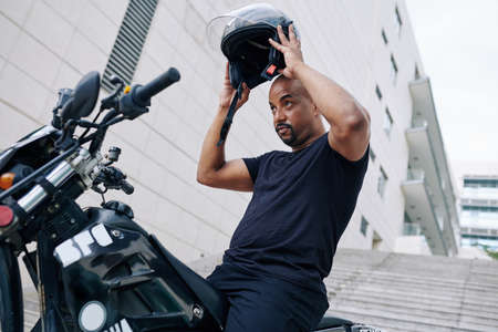 Serious muscular motorcyclist putting on helmet before riding through city streetsの写真素材
