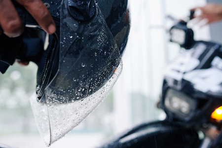 Close-up image of wet helmet glass with drops of water in hands of motorcyclist