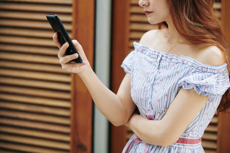 Cropped image of young pretty woman in summer dress checking text messages on smartphoneの写真素材